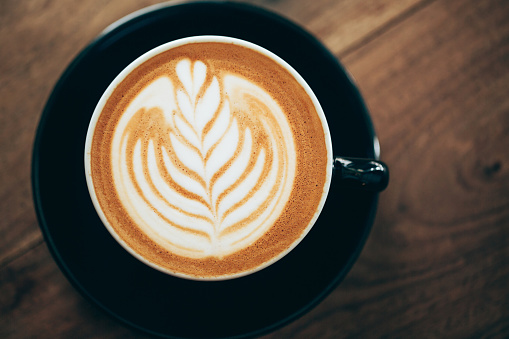 Red cup of cappucino with beautiful latte art on old wooden background. Top View.