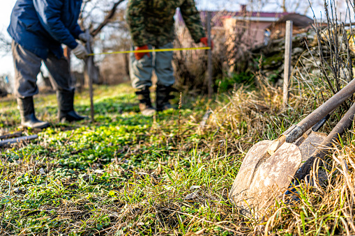 Men people with measuring tape working on vegetable winter garden for post raised bed cold frame in Ukraine dacha and closeup of shovel spade