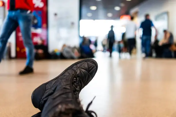 Inside modern airport low angle point of view with closeup of boots shoes on legs and many people waiting in hall corridor near gates