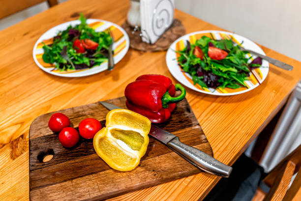 taglio di verdure sopra la vista sul tavolo da taglio con due piatti di insalata vegana fresca con peperoni gialli rossi e pomodori - 18635 foto e immagini stock