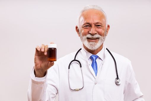 Portrait of senior doctor showing bottle of pills on gray background.