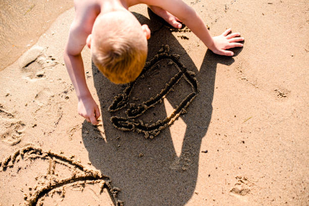 istock Top angle view of a little blond boy drawing in sand 1217413983