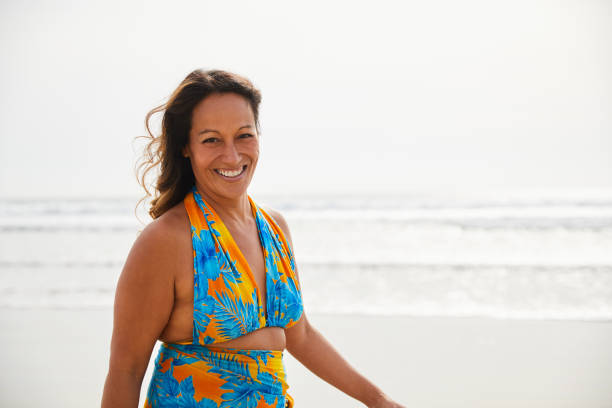 istock Laughing mature woman walking alone on a sandy beach 1217414959