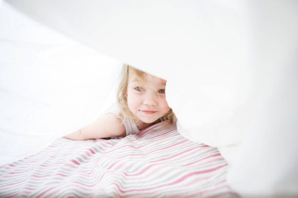 istock kid girl playing under blanket on bed. 1217416397