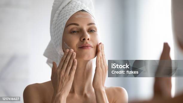 Smiling Young Pretty Lady Wrapped In Towel Smoothing Perfecting Skin Stock Photo - Download Image Now