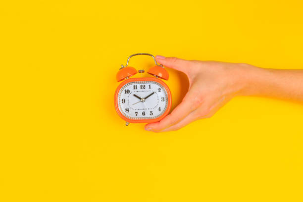 istock Beautiful young woman's hands with alarm clock  on pastel  background - Image 1217417297