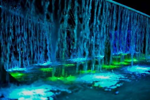 Fragment of the fountain as a background of vertical jets of water illuminated blue and green light, passing into turquoise.