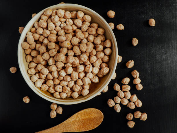 ceci in una ciotola di argilla, cucchiaio di legno su sfondo nero - legume bean chick pea sack foto e immagini stock