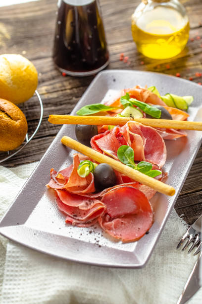 istock rustic wooden background, top and side, cold cuts, bacon and beef appetizer, fresh herbs, bread sticks and olives 1217423759
