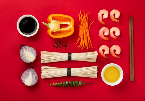 Asian noodles concept Ingredients for cooking stir fry noodles: noodles, shrimps, onion, cut carrot, bell pepper, chili, soy sauce, oil on red background. Top view, flat lay minimal design, Asian cuisine concept food state preparation shrimp prepared shrimp stock pictures, royalty-free photos & images
