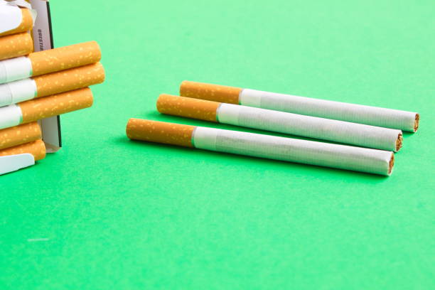 istock Three loose cigarettes next to a pack on the green table 1217428175
