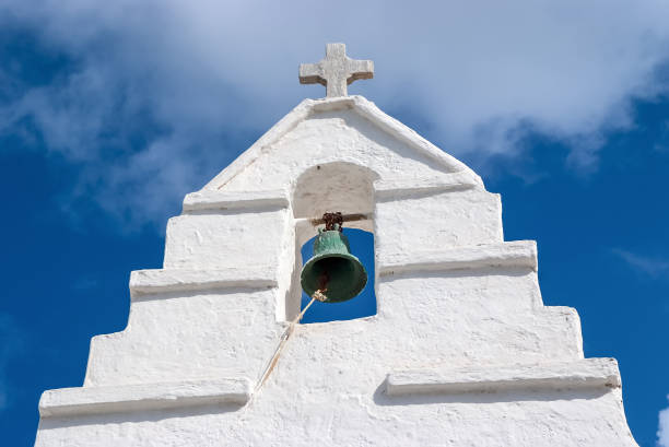 glockenturm mit kreuz in mykonos, griechenland. kapelle gebäude detail architektur. weiße kirche am wolkenverhangenen blauen himmel. religion und kultkonzept. sommerurlaub und reisen auf der mittelmeerinsel - church bell tower temple catholicism stock-fotos und bilder