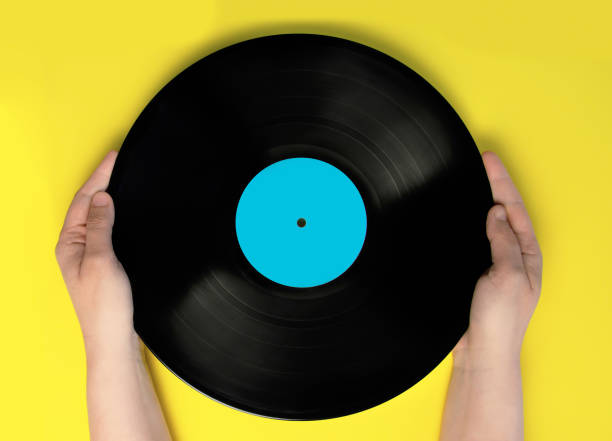 istock Woman's hands holding a vinyl record. Yellow background 1217439082
