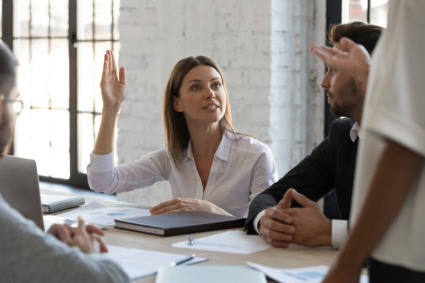 istock Serious ambitious businesswoman raise hand ask question to diverse presenter. 1217439270