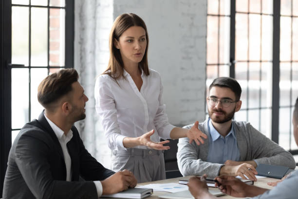 Attractive young mentor businesswoman conducts coaching in boardroom. Attractive young mentor businesswoman conducts coaching in boardroom at company meeting. Confidence woman training corporate team at briefing. Young employee share thoughts standing at table. bossy stock pictures, royalty-free photos & images