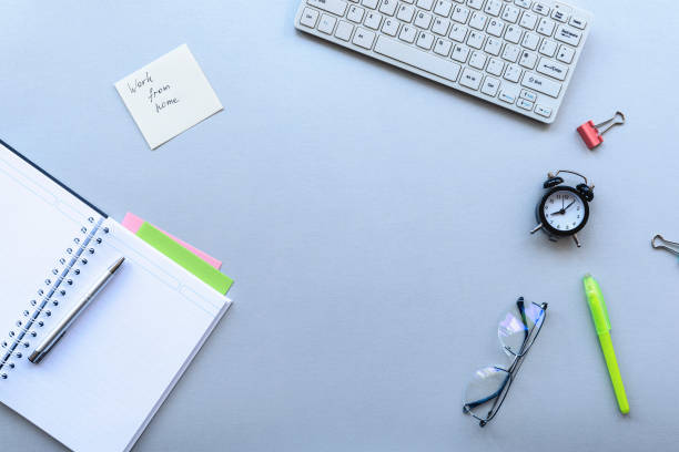 istock Cozy workplace with keyboard, notepad, alarm clock and glasses on grey background. Work from home concept 1217444397