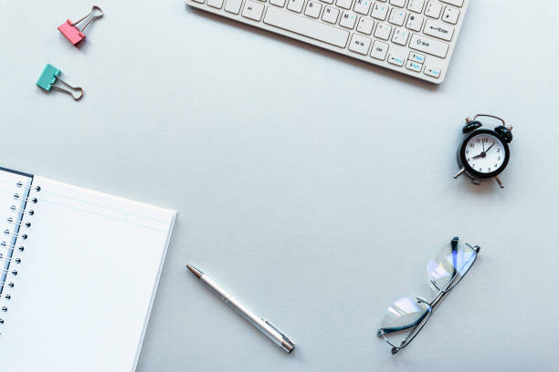 istock Work space table with laptop, notepad, alarm clock, pen and glasses on grey background 1217444578