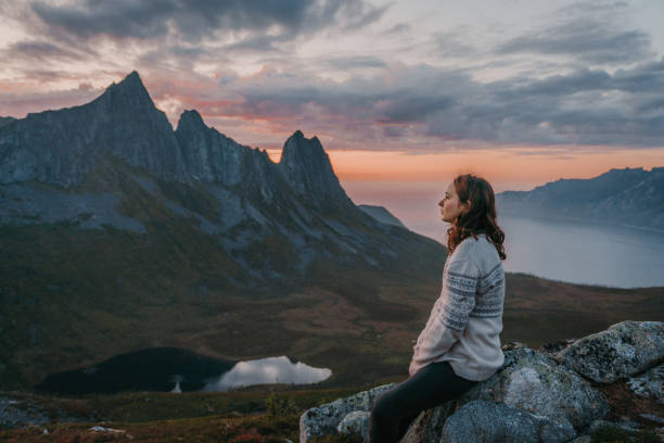 istock Woman sitting and looking at Segla mountain on Senja island 1217444834