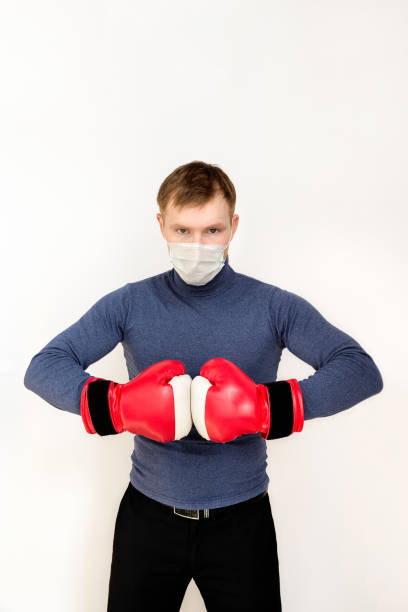 junger mann in roten boxhandschuhen auf weißem, isoliertem hintergrund. sein ausdruck ist bedrohlich und entschlossen. auf seinem gesicht hat er eine medizinische maske, die vor viren, verschmutzung, coronavirus und infektionen schützt. - immune defence stock-fotos und bilder