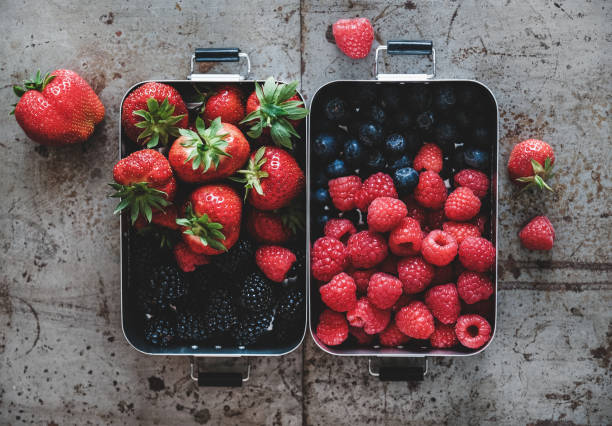 istock Flat-lay of fresh berries in lunchboxes over rough grey background 1217446247