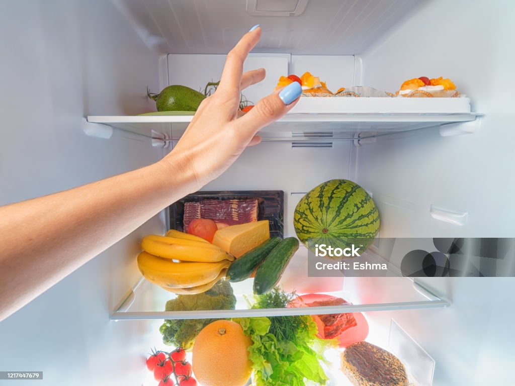 Woman hand picking something from a full open fridge Woman hand picking something from a full open fridge. First person view Refrigerator Stock Photo