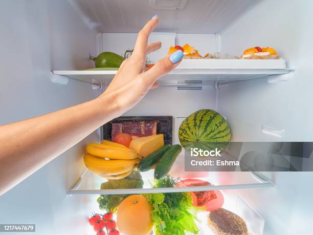 Woman Hand Picking Something From A Full Open Fridge Stock Photo - Download Image Now
