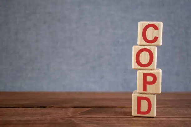 Photo of Abbreviation COPD (Chronic Obstructive Pulmonary Disease) text acronym on wooden cubes on dark wooden backround. Medicine concept.