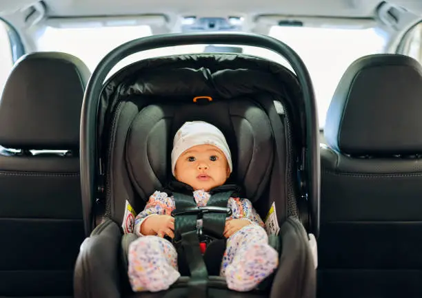 A 3 month old baby sitting in a carseat in the backseat of an auto.