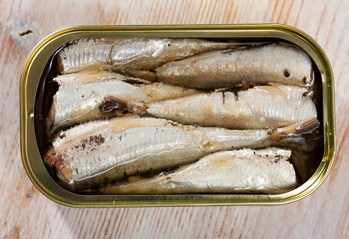 Opened can of sardines preserves in oil on wooden table