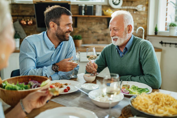 istock Happy senior man and his son toasting with wine at dining table. 1217450743