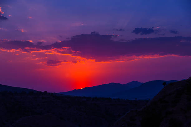 Stunning sunset in the mountains. Bright backlit sky and clouds. Silhouettes of mountain peaks in the rays of the sun. Incredible wallpaper