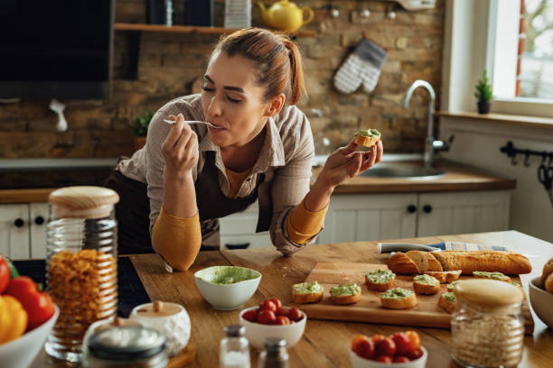 young woman eating while making avocado bruschetta in the kitchen. - tasting imagens e fotografias de stock