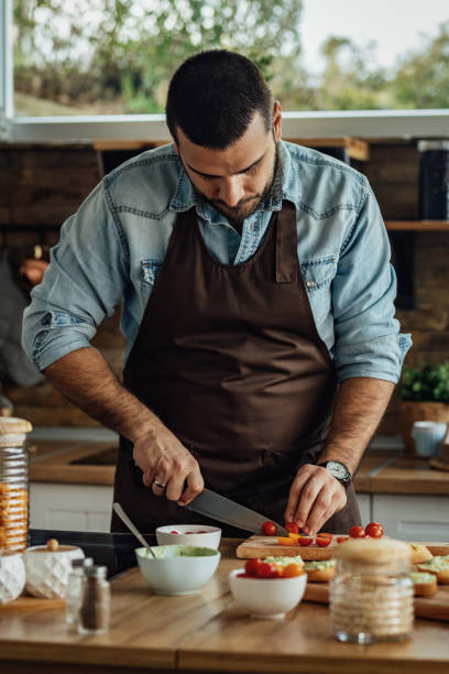 istock Young man slicing cherry tomato in the kitchen. 1217452101