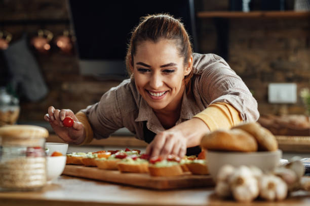 istock Happy woman adding cherry tomato while making bruschetta in the kitchen. 1217452329