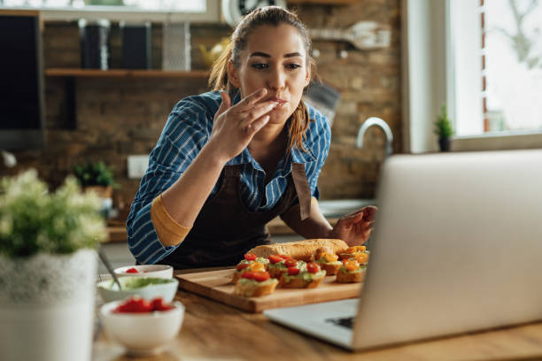 istock Young happy woman using laptop while preparing bruschetta in the kitchen. 1217452603