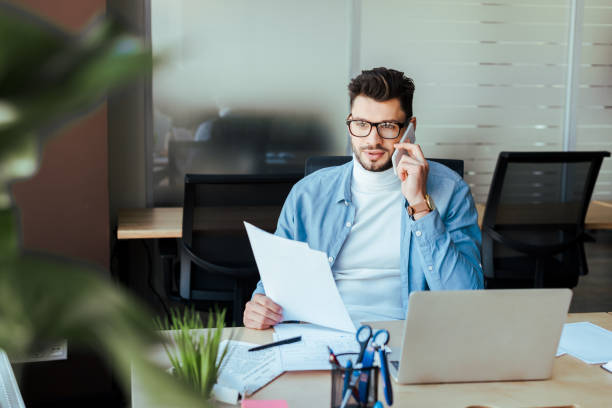 istock Selective focus of IT worker with papers talking on smartphone at table in coworking space 1217453648