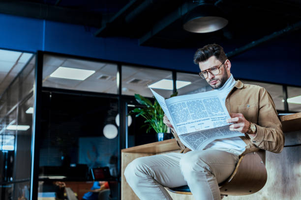 istock Low angle view of IT worker reading newspaper on chair in coworking space 1217453652