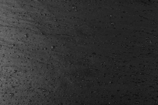 Wet black slate stone, food slate, slab surface, plate stone texture background. Chalkboard, graphite board, rock, slab rock pattern with water drops