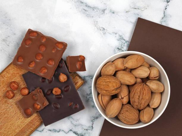 istock Broken chocolate bars and raw nuts on gray marble background 1217462570