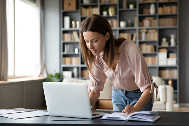 istock Pleasant young woman working on laptop, standing at table. 1217463762