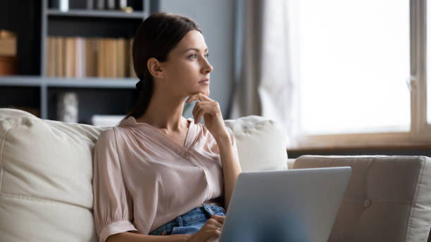 Distracted from work young woman sitting on couch with laptop. Distracted from work worried young woman sitting on couch with laptop, thinking of problems. Pensive unmotivated lady looking at window, feeling lack of energy, doing remote freelance tasks at home. wasting time stock pictures, royalty-free photos & images