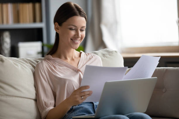 istock Smiling young woman sitting on sofa, reading paper letters. 1217463825