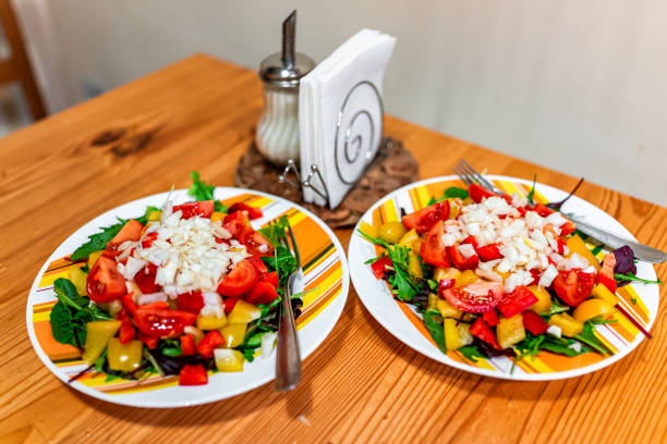 dos platos de ensalada vegana con pimientos amarillos rojos, cebollas y tomates en la mesa con tenedor, salero de sal y servilleta - 18638 fotografías e imágenes de stock