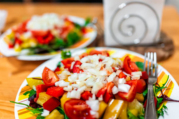 macro closeup of two plates of vegan salad with red yellow bell peppers, onions and tomatoes on table with fork and napkin holder - 18639 imagens e fotografias de stock