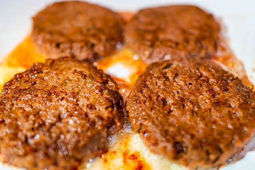 Four vegan burgers plant-based patties cooking frying on ceramic frying pan macro closeup showing texture of meat substitute