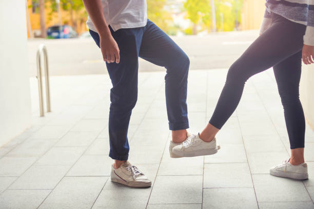 Man and woman practicing social distancing outdoors. They are doing an foot bump shake greeting. Both are casually dressed.