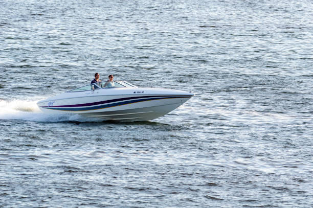Couple in sleek boat crossing New Bedford outer harbor New Bedford, Massachusetts, USA - September 2, 2018: Sport boat gliding across chop in New Bedford outer harbor in early evening racing boat photos stock pictures, royalty-free photos & images