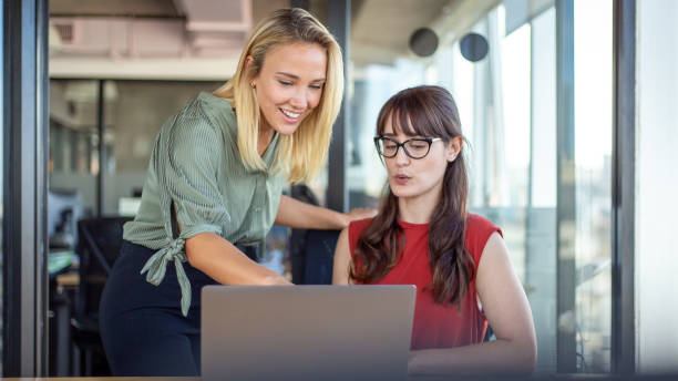 istock Blonde female office worker smiling while looking at colleague's computer 1217477687