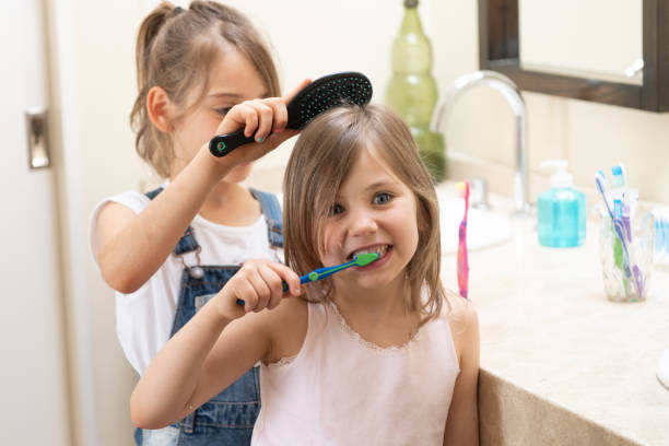 istock Young girl brushing her teeth while her sister brushes her hair 1217477696