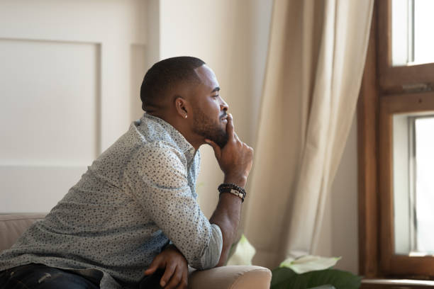 istock Pensive african man sitting on couch looking out the window 1217477762